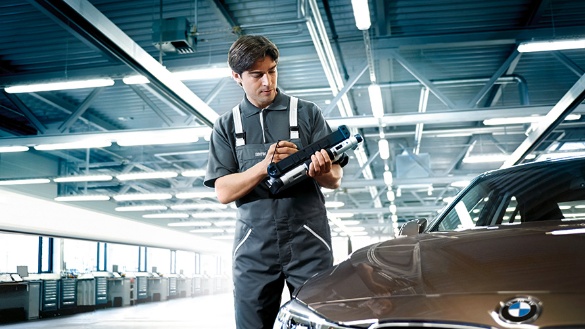 Mechaniker in Werkstatt prüft Gerät neben braunem BMW.