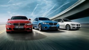 Drei BMW-Autos in Rot, Blau und Weiß fahren nebeneinander auf einer Straße unter einer Brücke.