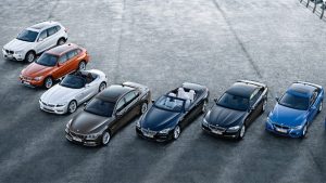 Acht BMW-Fahrzeuge in verschiedenen Farben auf grauem Asphalt geparkt.