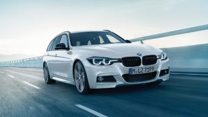 Weißer BMW auf Autobahn bei Tageslicht, frontal aufgenommen, klare blaue Himmel im Hintergrund.