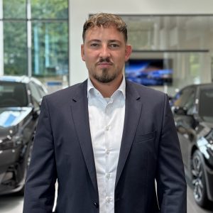 Ein Mann im Anzug steht in einem BMW-Autohaus, umgeben von Fahrzeugen.