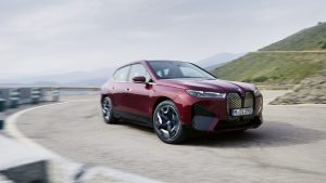 Roter BMW iX fährt auf einer kurvigen Straße mit Berglandschaft im Hintergrund.