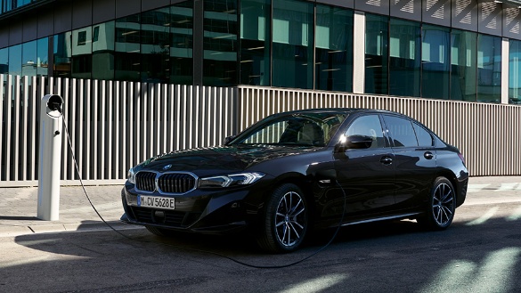 Schwarzer BMW 3er an Ladestation vor modernem Gebäude bei Sonnenschein.