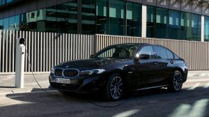 Schwarzer BMW 3er-Limousine beim Laden an einer Ladestation vor moderner Gebäudeumgebung.
