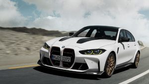 Weißer BMW M3 fährt dynamisch auf einer Straße, blauer Himmel im Hintergrund.