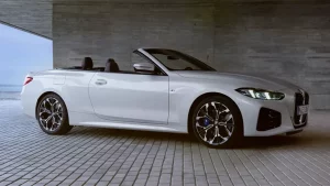 Weißes BMW 4er Cabrio auf gepflastertem Boden vor Betonwand, Verdeck offen, keine Personen sichtbar.