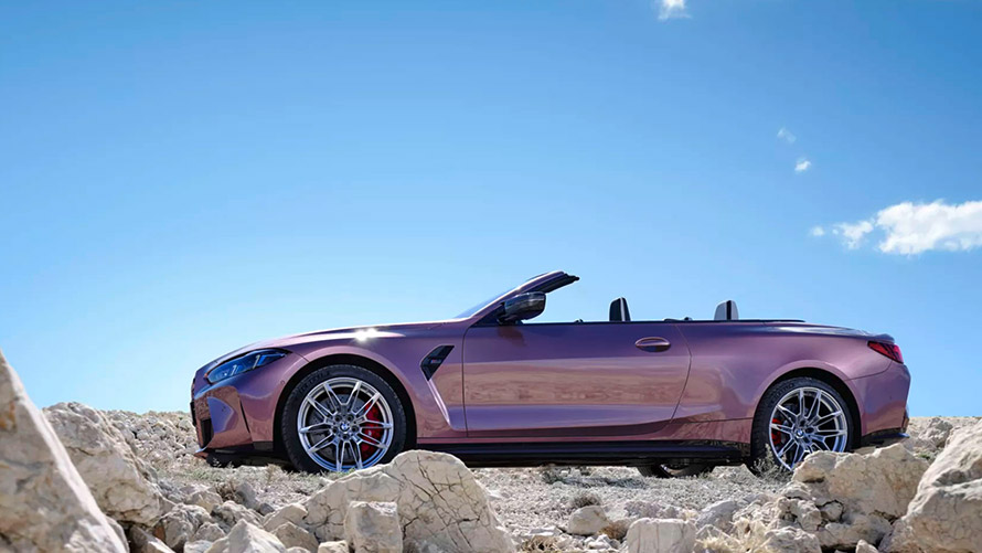BMW 4er M Cabrio in Lila steht zwischen Felsen unter klarem Himmel.