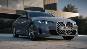 Graues BMW 4er Gran Coupé, Frontansicht, auf gepflastertem Platz vor modernem Gebäude.