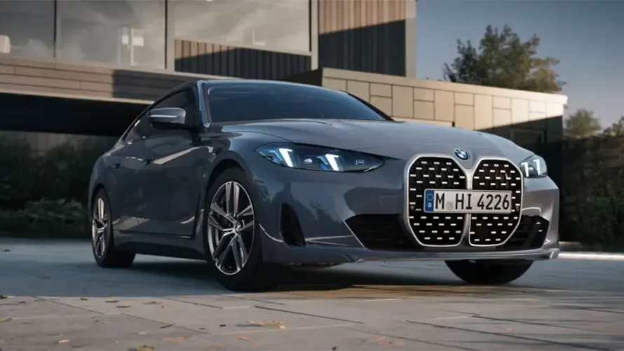 Graues BMW 4er Gran Coupé, Frontansicht, auf gepflastertem Platz vor modernem Gebäude.