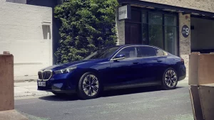 Blauer BMW 5er Limousine vor einem Gebäude mit Glasfront und Pflanzen im Hintergrund.