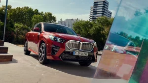 Roter BMW iX2 parkt auf einer Straße vor grünen Bäumen und modernen Gebäuden.