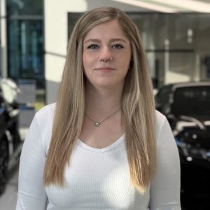 Eine Frau mit langen blonden Haaren in einem Autohaus. Im Hintergrund sind Autos zu sehen.