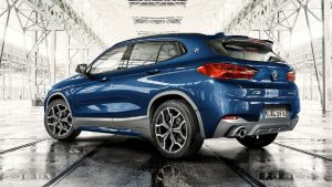 Blauer BMW X2 in heller Halle, seitlich von hinten fotografiert, auf Schienen stehend.