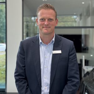 Ein Mann im Anzug mit Namensschild steht in einem modernen Büro mit Glaswänden.