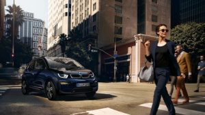 Eine Frau und ein BMW i3 auf einer Stadtstraße bei Sonnenschein.