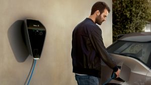 Mann lädt BMW i3 an einer Wandladestation im Freien auf.