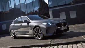 Grauer BMW 1er parkt vor modernem Gebäude auf gepflastertem Gehweg.