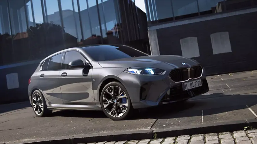 Grauer BMW 1er parkt vor modernem Gebäude auf gepflastertem Gehweg.