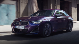 Lila BMW 2er Coupé fährt auf einer Straße, Gebäude im Hintergrund.