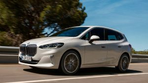 Silberner BMW 2er Active Tourer fährt auf einer Straße, umgeben von Bäumen und blauem Himmel.