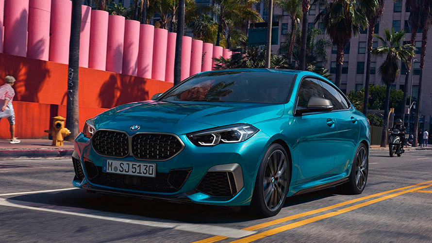 Türkises BMW 2er Coupé fährt auf Stadtstraße, im Hintergrund Palmen und bunte Mauer.