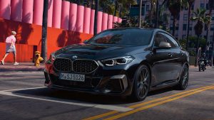 Schwarzes BMW 2er Gran Coupé fährt auf urbaner Straße, Palmen und bunte Wand im Hintergrund.