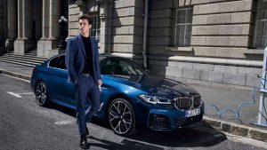 Ein blauer BMW steht neben einem Mann in einem Anzug vor einem historischen Gebäude.