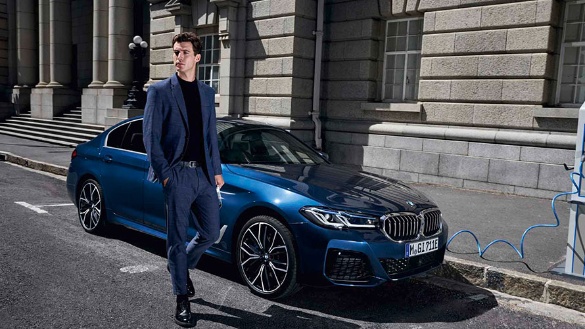 Ein blauer BMW steht neben einem Mann in einem Anzug vor einem historischen Gebäude.