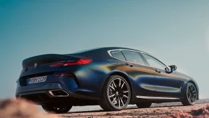 Blaues BMW 8er Gran Coupé auf einer staubigen Straße unter klarem Himmel, von hinten fotografiert.