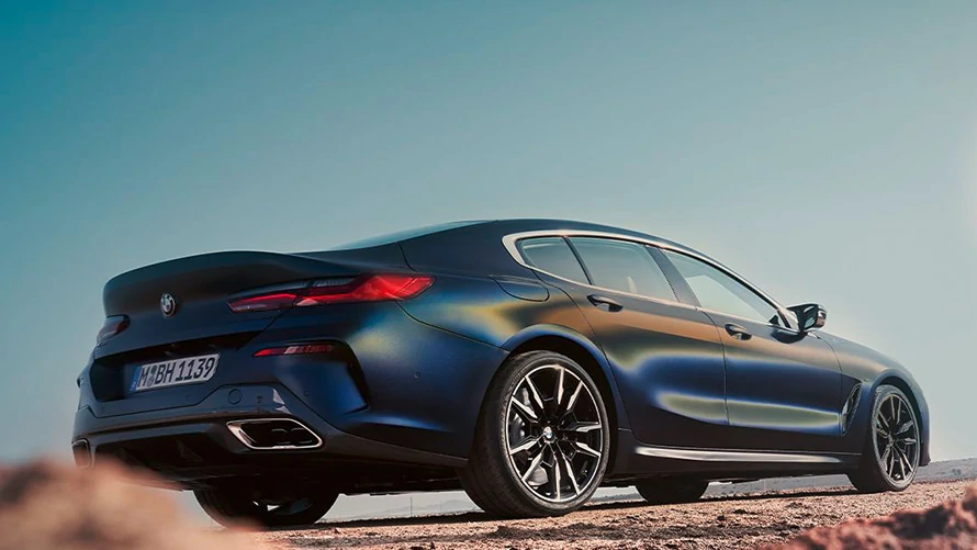 Blaues BMW 8er Gran Coupé auf einer staubigen Straße unter klarem Himmel, von hinten fotografiert.