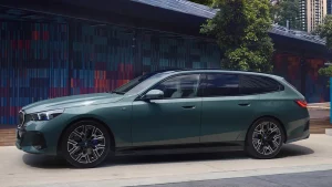 Grüner BMW Kombi, seitlich, vor modernem Gebäude mit bunten Wänden und Bäumen.