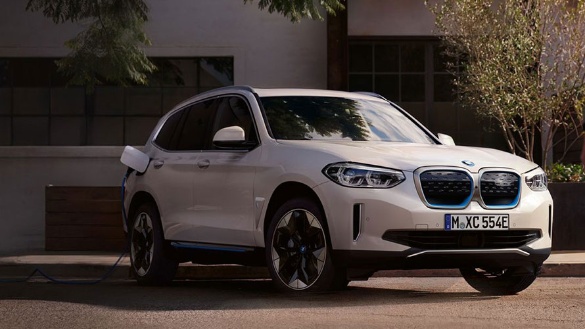 Weißer BMW SUV mit blauen Akzenten, parkt draußen, Bäume im Hintergrund.