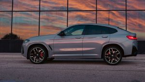 Silberner BMW X4 vor Glasfassade bei Sonnenuntergang, seitliche Ansicht.