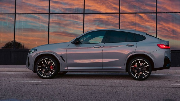 Silberner BMW X4 vor Glasfassade bei Sonnenuntergang, seitliche Ansicht.