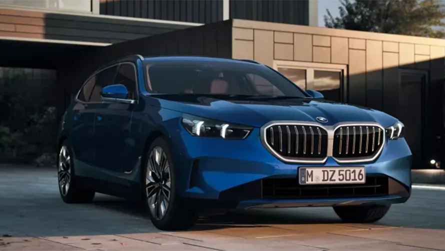 Blauer BMW 5er Touring 2024 vor modernem Gebäude, frontal aufgenommen.