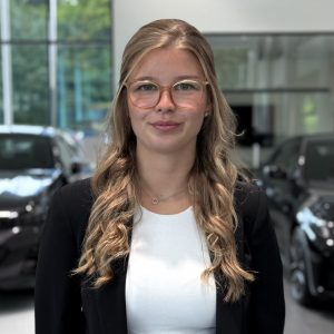 Eine Frau mit Brille in einem Autohaus, im Hintergrund stehen schwarze Autos.