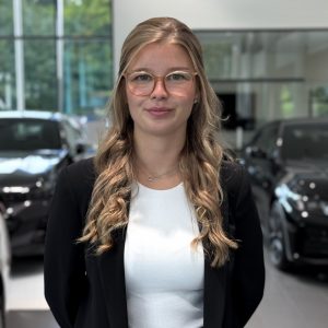 Frau mit Brille in Autohalle, im Hintergrund schwarze Autos.