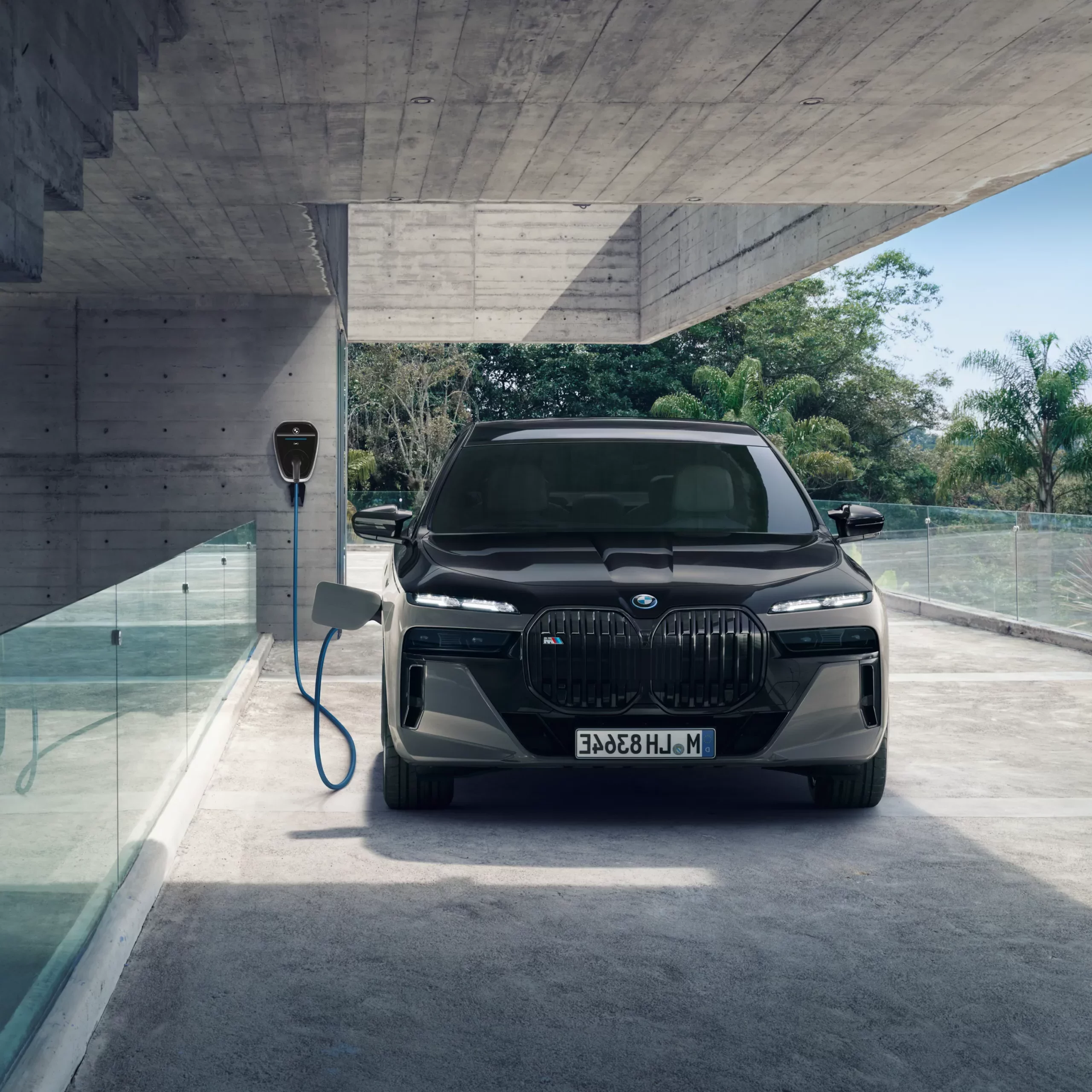 Schwarzer BMW lädt an einer Wallbox in moderner Garage mit Glaswand und Betonoptik.