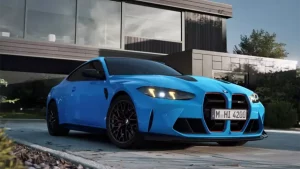 Blauer BMW M vor modernem Gebäude bei Tageslicht, mit Bäumen im Hintergrund.