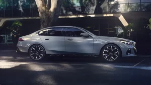 Silberner BMW i5 in Seitenansicht vor einem modernen Gebäude mit Bäumen.