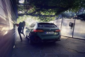 Grünes BMW-Auto lädt an einer Wandladestation, daneben eine Person in schwarzer Kleidung.