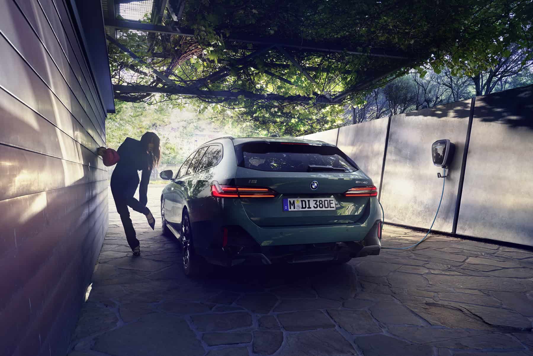 Grünes BMW-Auto lädt an einer Wandladestation, daneben eine Person in schwarzer Kleidung.