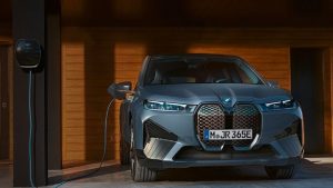 Silberner BMW iX M60 parkt in Garage, wird an Ladestation angeschlossen.