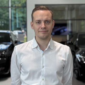 Mann in weißem Hemd steht in einem Autohaus vor schwarzen Autos.