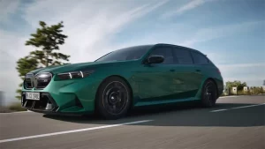 Grüner BMW Kombi fährt auf offener Straße, Bäume und Himmel im Hintergrund.