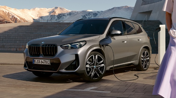 Graues BMW-SUV beim Laden an einer Ladestation vor bergiger Kulisse.