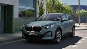 BMW X2 in Blau auf Straße, modernes Gebäude und Bäume im Hintergrund, bei Tageslicht.