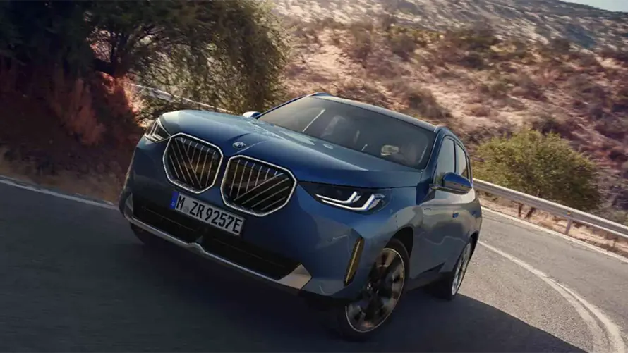 Blauer BMW SUV fährt auf kurviger Straße in sonniger, trockener Landschaft.