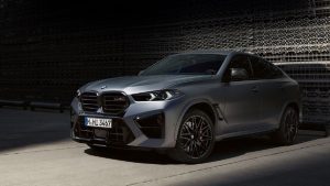 Silberner BMW X6 M auf einem Parkplatz, seitliche Frontansicht, teils im Schatten.