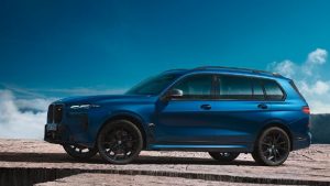 Blauer BMW X7 SUV auf felsigem Untergrund vor einem bewölkten Himmel.